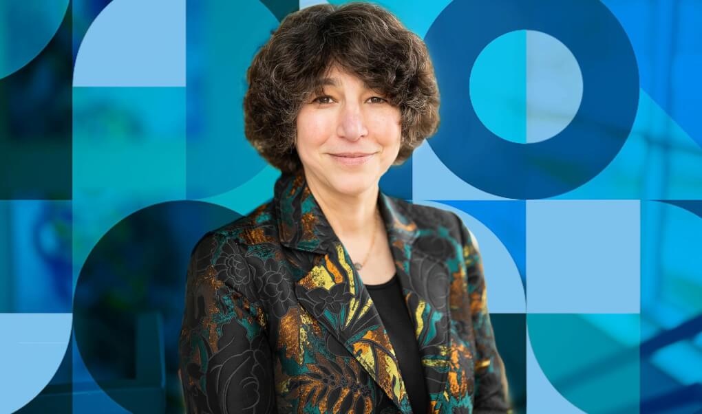 Lesley Slavit wears a yellow, orange, teal and black floral jacket and a pattern of teal, blue and navy circles, squares and triangles is overlaid on top of the photo in the background.